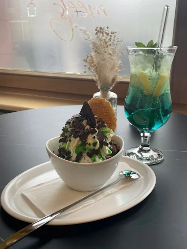 Eisbecher mit Schokoraspeln und Waffel neben einem blauen Mocktail