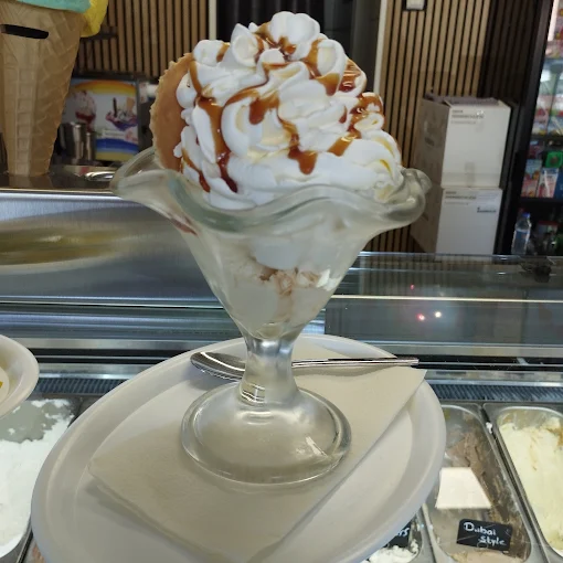 Großer Eisbecher mit Sahne und Karamellsauce vor der Eistheke